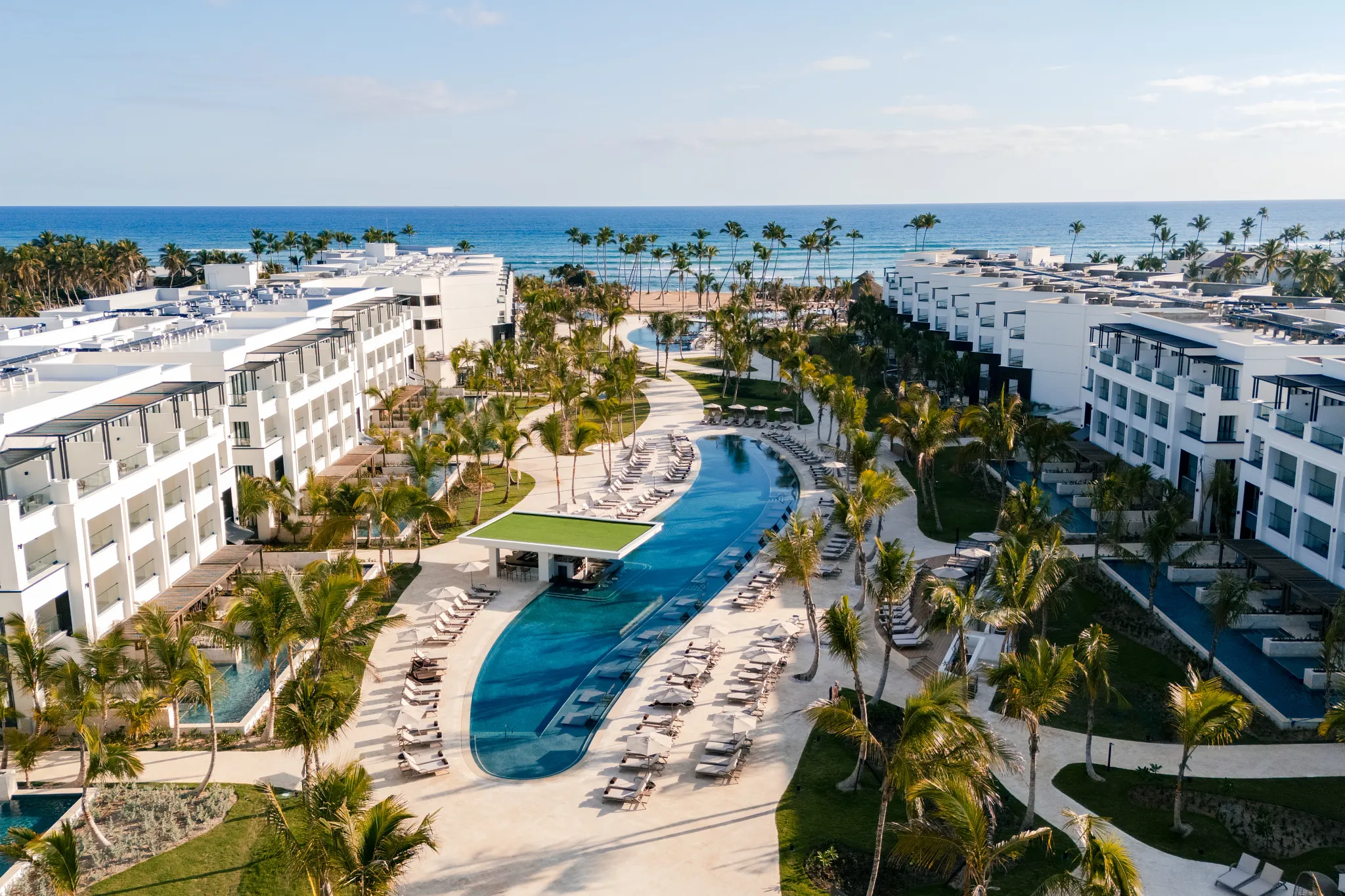 Wide aerial view of Secrets Tides Punta Cana resort buildings, pools, and tropical gardens facing the ocean.